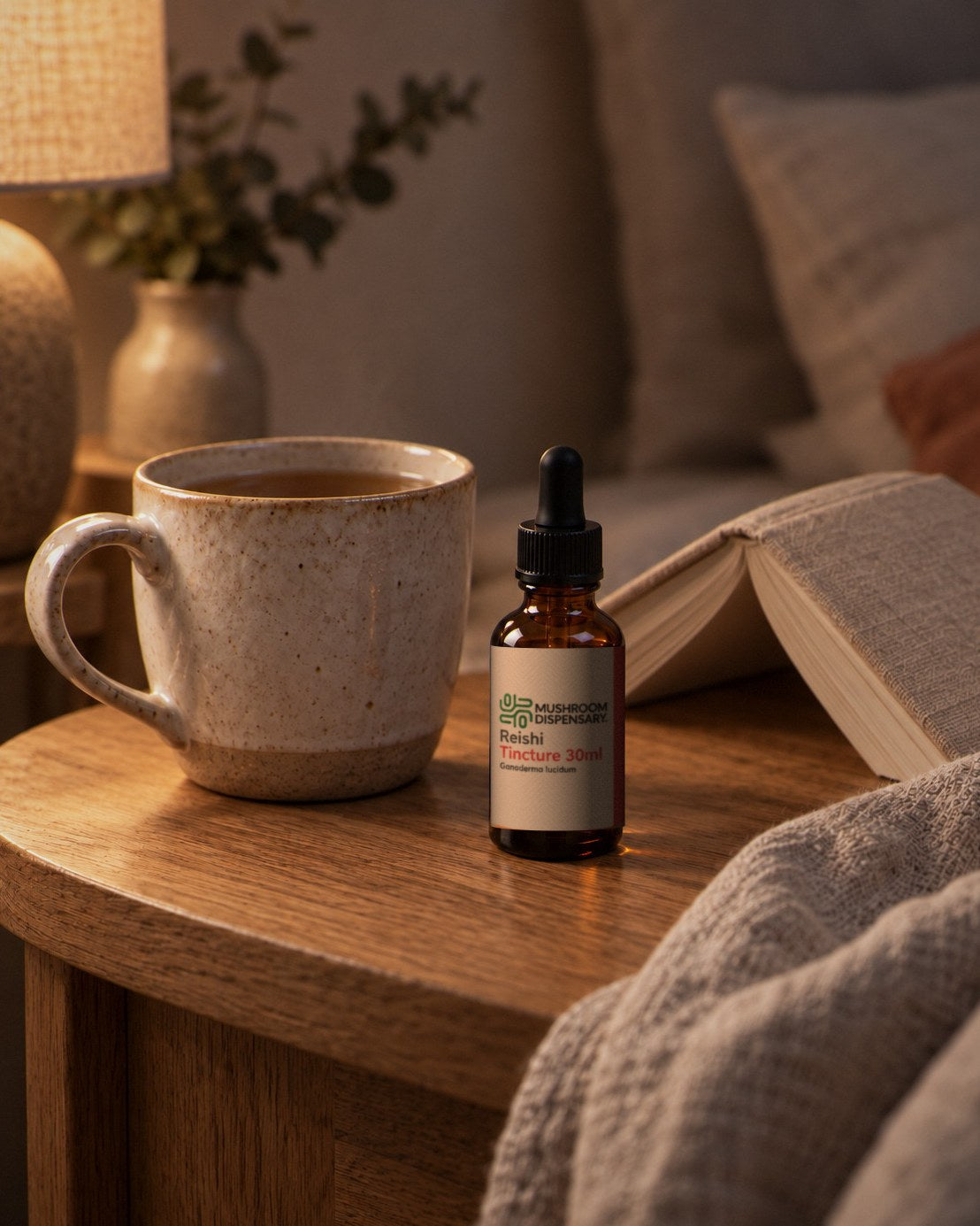 A mug of tea and a Mushroom Dispensary Reishi Tincture 30ml bottle on a side table under a warm evening lamp