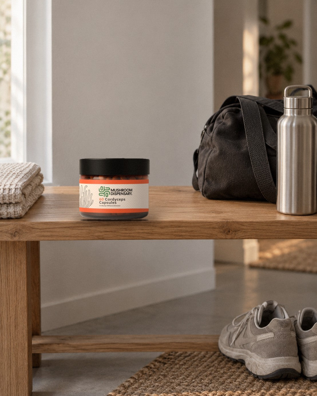 A jar of Mushroom Dispensary Cordyceps Capsules on an oak bench beside a gym bag and a steel water bottle, trainers below